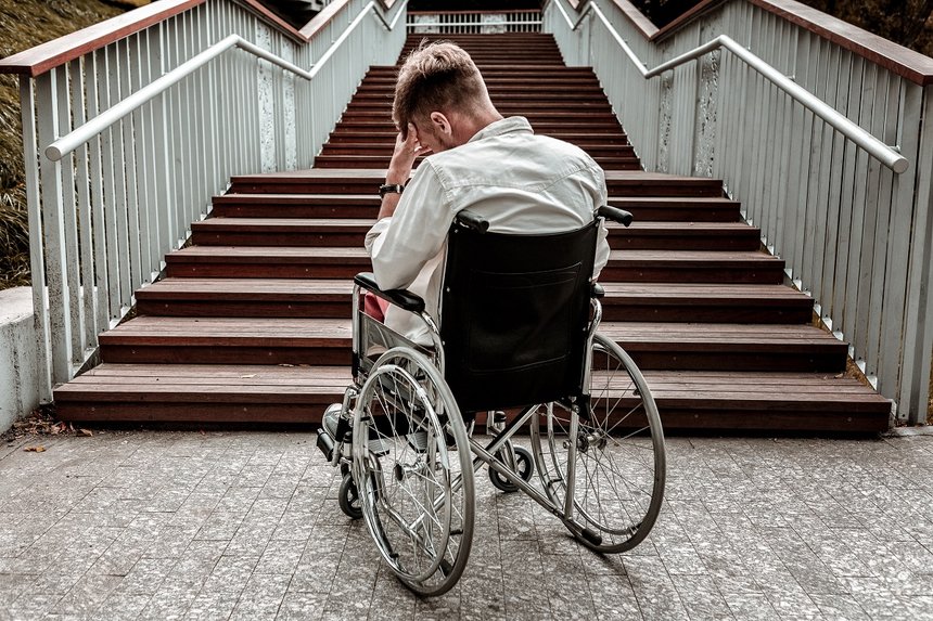 Many stairs. Horizontal image of depressed disabled man sitting in the wheelchair and facing the difficulties with climbing the stairs alone