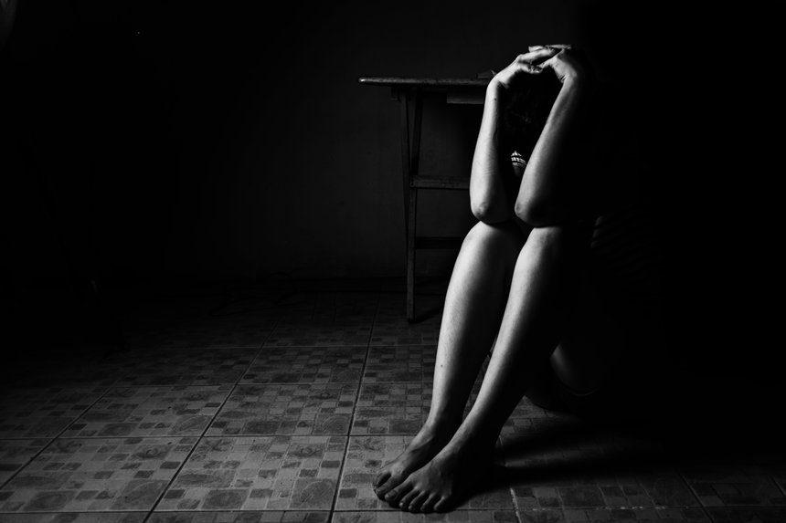 a woman sitting on ground with arm around lower head, sexual violence , sexual abuse, human trafficking concept