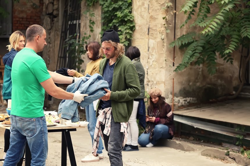 Volunteers giving clothes and food to homeless people outdoors