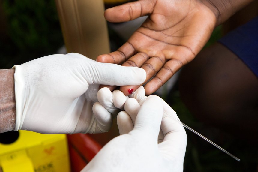 a health worker doing a finger prick test for HIV. He is drawing blood into a capillary tube after pricking the patient with a lancet. Photo taken in Uganda in 2017.