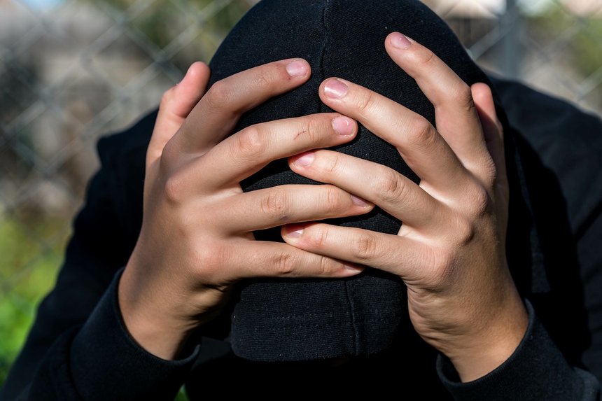Young unidentifiable teenage boy  holding hes head at the correctional institute , conceptual image of juvenile delinquency, focus on the boys hand.