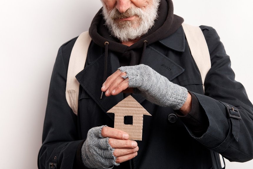 unrecognizable old man wearing street clothes holding house made of cardboard, dream about shelter. Isolated over white background