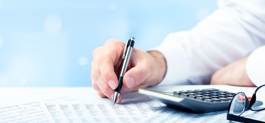 Business Man Using Pen And Calculator On Desk With Reading Glass