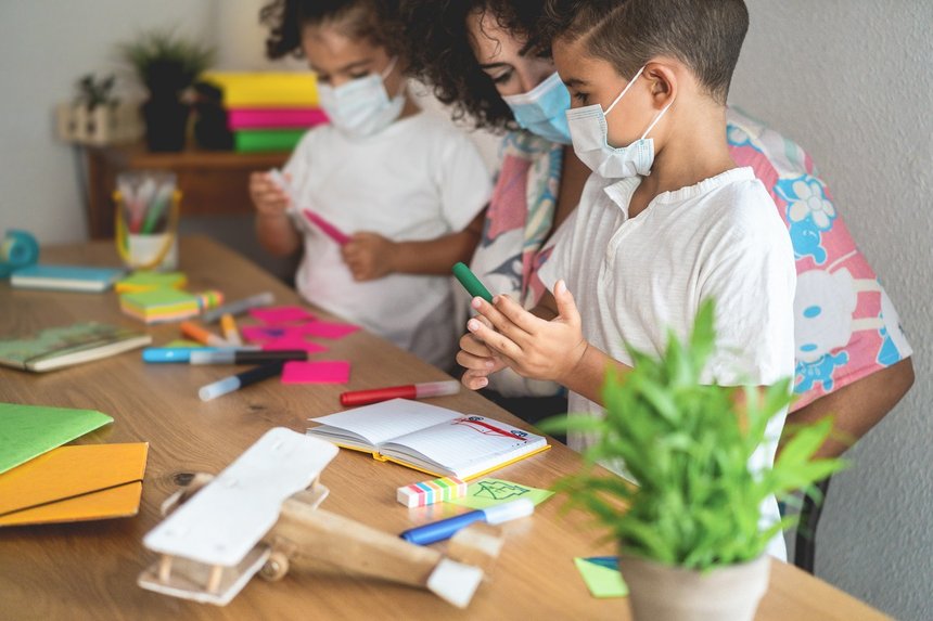 School teacher helping children in classroom while wearing safety masks  during coronavirus outbreak- Focus on boy's face