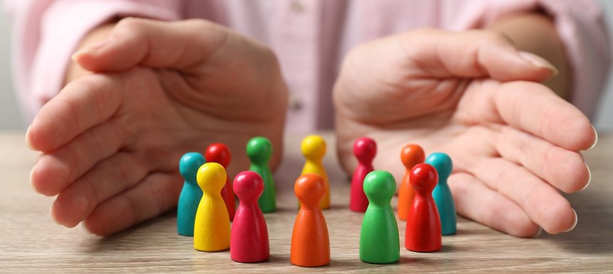 Woman protecting colorful pawns at wooden table, closeup. Divers