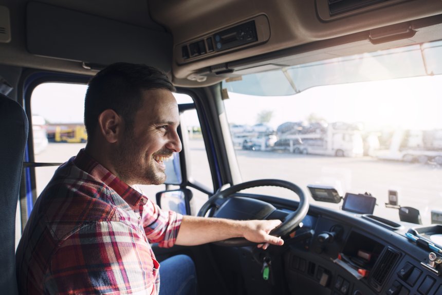 Professional middle aged truck driver in casual clothes driving truck vehicle going for a long transportation route.