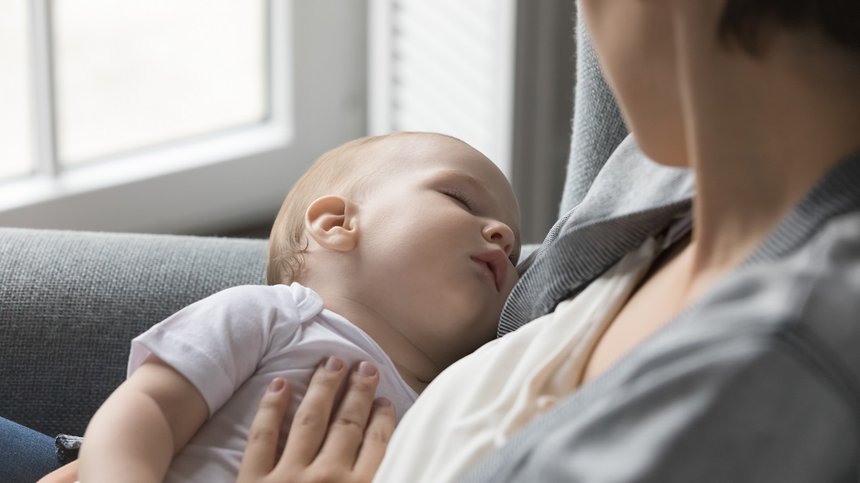 Close up loving mother holding sleeping cute newborn baby in arms, lulling newborn, looking at child with love, enjoy moment of tenderness, relax seated on armchair at home. Babyhood, happy motherhood