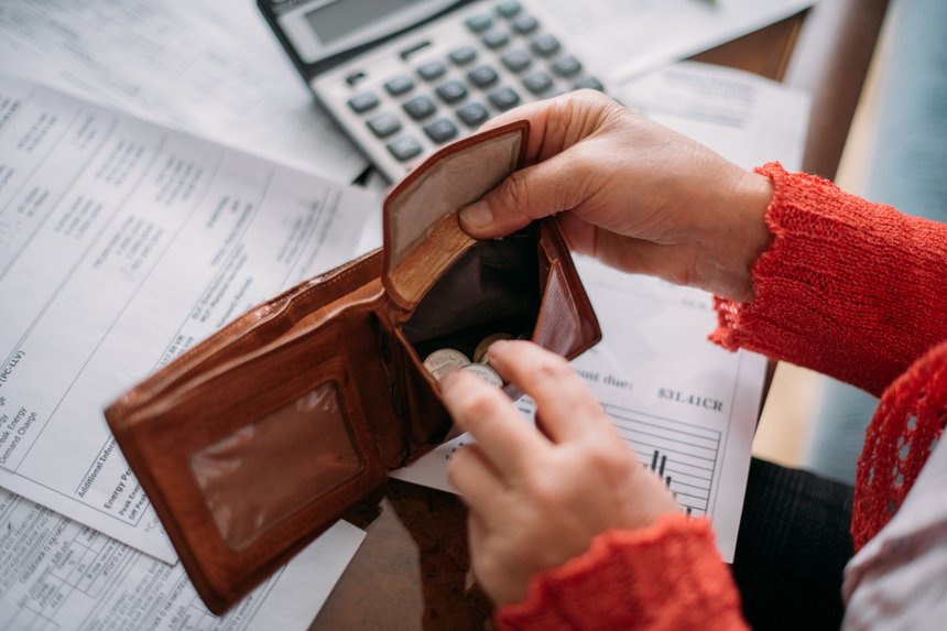 The hands of an elderly woman with an empty wallet and a lot of utility bills.