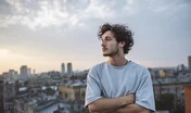 young migrant man standing on a rooftop in a new city, looking over the skyline