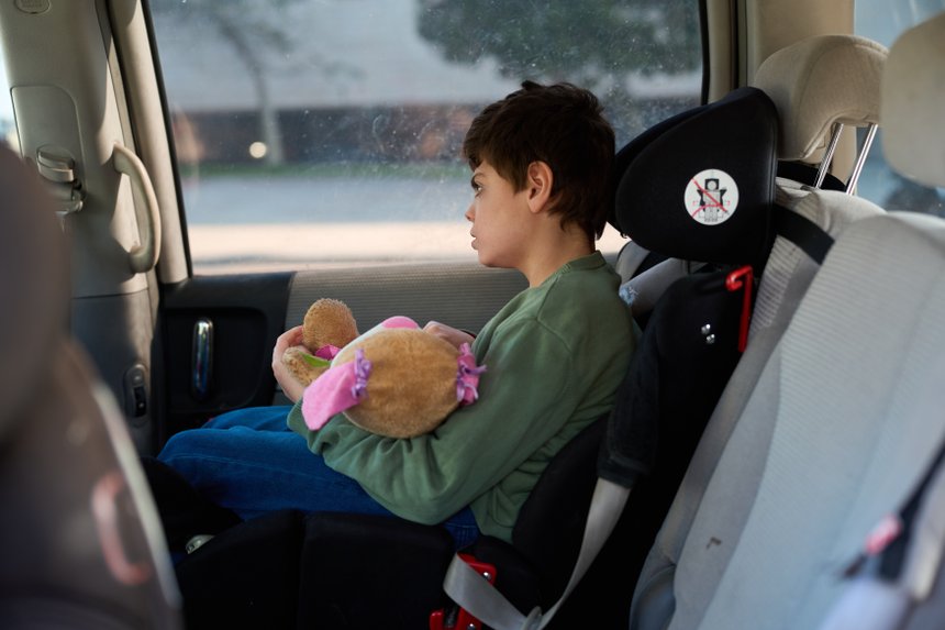 Boy with disability holding teddy bear while traveling by car
