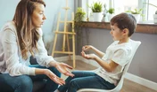 Family concept, mother and son relationship, happy young boy holding a teddy bear and talking to his mother. Smiling young woman talking to boy in white room