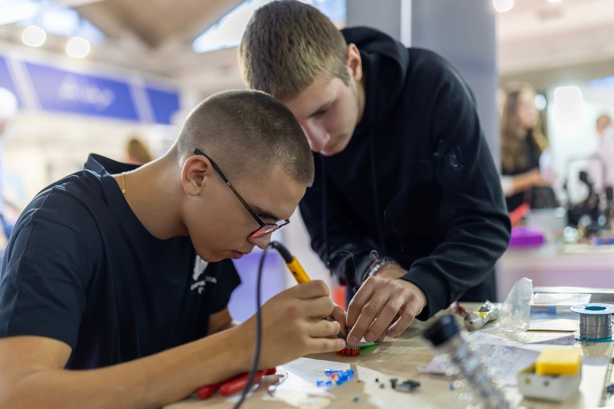Young men learning electronics soldering skills in workshop