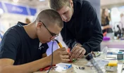 Young men learning electronics soldering skills in workshop